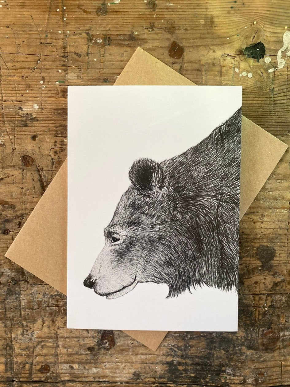 Hand drawn bear on a white greeting card  that's blank inside. The card has a brown envelope behind it and is placed on a rustic table.