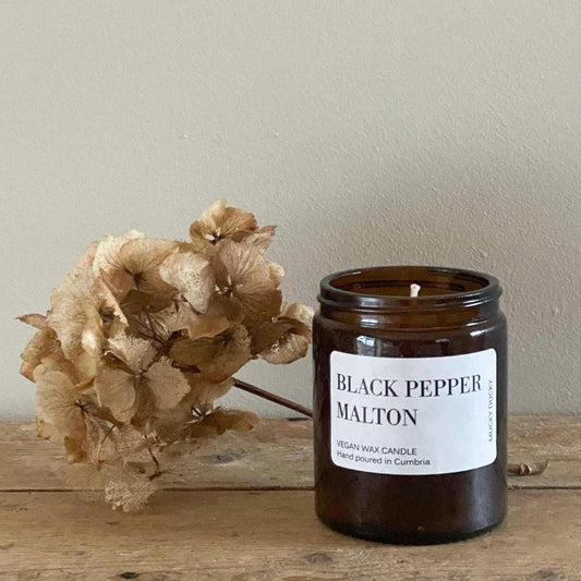 Handpoured Black Pepper Malton candle in an amber glass jar with a dried flower behind it